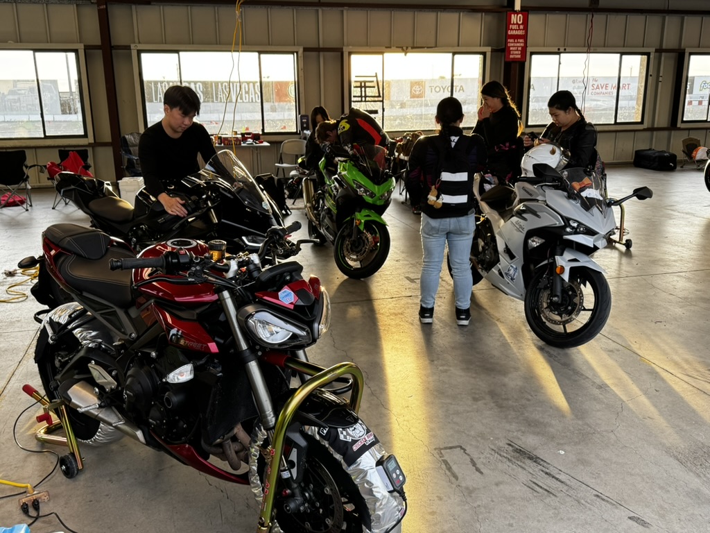 Riders and motorcycles set up in a track paddock garage.